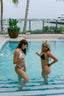 Two women in swimsuits standing in a pool with a scenic background