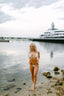 Woman in a bikini standing on a beach with a yacht in the background