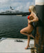 Woman in a red bikini leaning against a pole with a yacht in the background