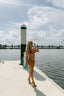 Woman in a red bikini standing on a dock with water and sky in the background
